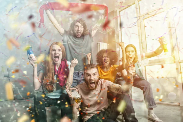 Felices amigos de los aficionados al fútbol viendo el fútbol en la televisión y celebrando la victoria con confeti cayendo . —  Fotos de Stock