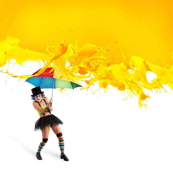 Clown with umbrella covers himself from yellow color drops — Stock Photo, Image