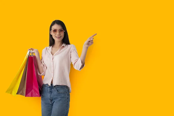 Happy woman with shopping bags in hand indicates something — Stock Photo, Image