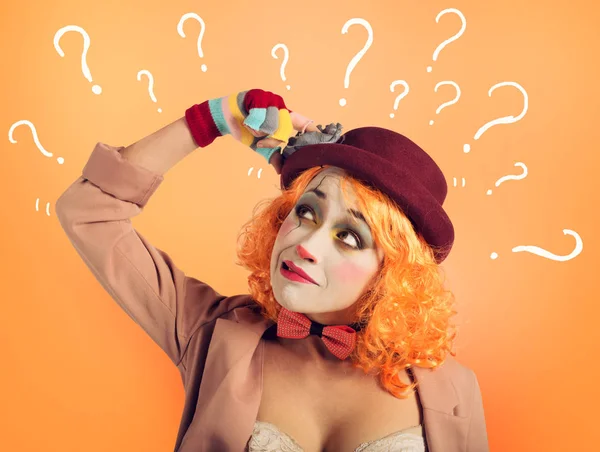 Pensive clown meisje met te veel vragen. Oranje achtergrond — Stockfoto