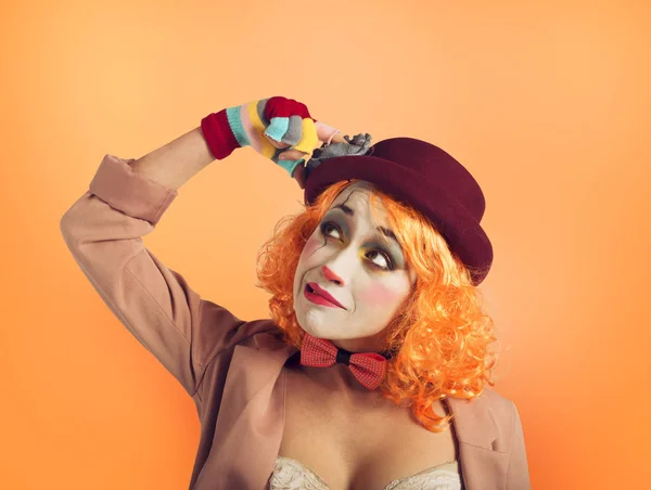 Nachdenkliches Clownmädchen mit zu vielen Fragen. orangen Hintergrund — Stockfoto