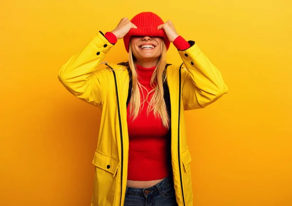 Девушка в куртке на жёлтом фоне покрывает лицо шляпой на погоду — стоковое фото