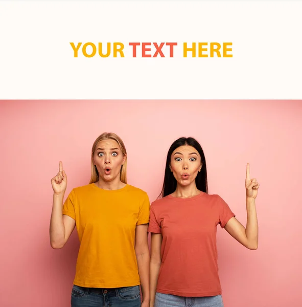 Two girls indicates something. Amazed expression face. Pink background with blank space for your text — Stock Photo, Image