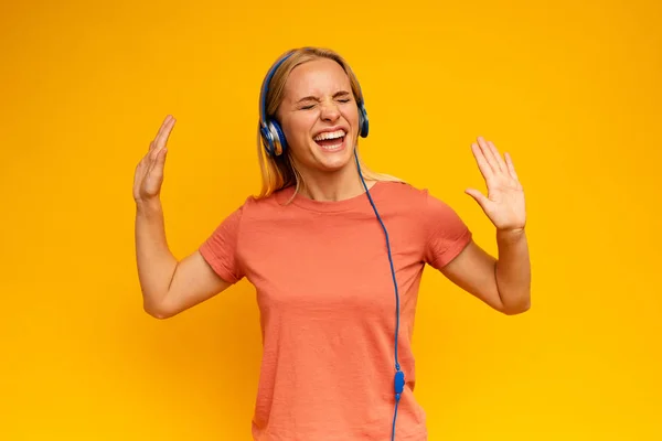 Blonde girl listens to music with headset. Joyful expression on yellow background — Stock Photo, Image