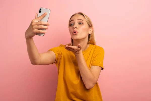 Rubia linda chica envía corazones en su teléfono inteligente. Cara de expresión feliz y encantadora. Fondo rosa — Foto de Stock