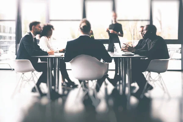 Έννοια υποβάθρου με επιχειρηματίες που κάθονται στο τραπέζι συνεδριάσεων στο γραφείο κοντά σε ένα τζάμι παραθύρου — Φωτογραφία Αρχείου