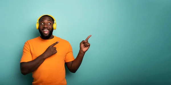 Ragazzo con auricolare giallo ascolta musica e indica qualcosa — Foto Stock