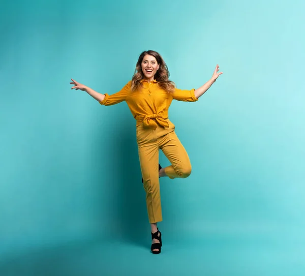 Menina morena com uma roupa amarela salta sobre um fundo ciano. Conceito de moda e compras com expressão alegre — Fotografia de Stock