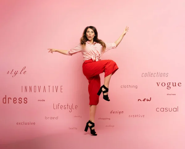 Chica morena con ropa roja salta sobre un fondo rosa con términos de moda. Concepto de moda y compras con expresión alegre — Foto de Stock