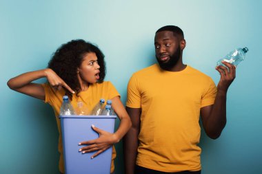 Mutlu çift açık mavi renkli bir şişenin üzerinde plastik bir kap tutuyor. Ekoloji, koruma, geri dönüşüm ve sürdürülebilirlik kavramı