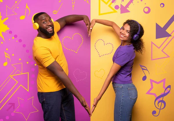 Casal com fone de ouvido ouvir música e fazer a forma do coração com os braços. fundo violeta e amarelo — Fotografia de Stock