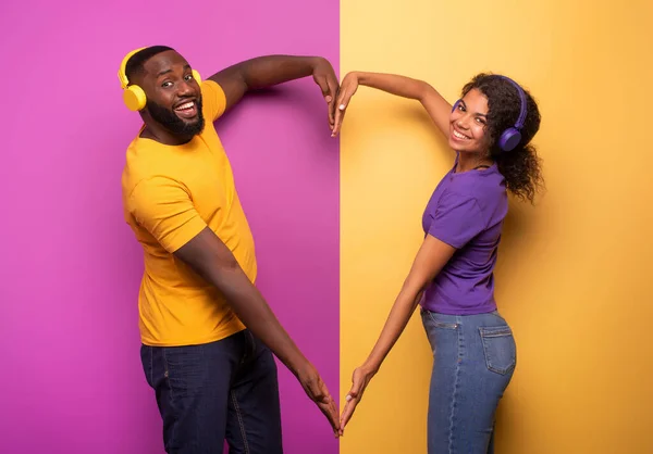 Pasangan dengan headset mendengarkan musik dan membuat bentuk hati dengan tangan. latar belakang ungu dan kuning — Stok Foto