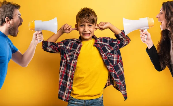 Child covers his ears because he does not want to hear the cries and reproaches of his parents. Yellow background — Stock Photo, Image