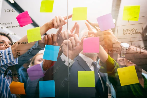 Une équipe de personnes au travail dans le bureau indique avec leur main un post-it sur le verre — Photo