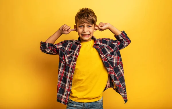 Kind bedekt zijn oren omdat hij geen geluid wil horen. Gele achtergrond — Stockfoto