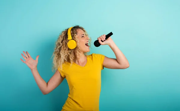 Chica con auriculares escucha música y canción con micrófono. expresión emocional y energética. Antecedentes cian — Foto de Stock