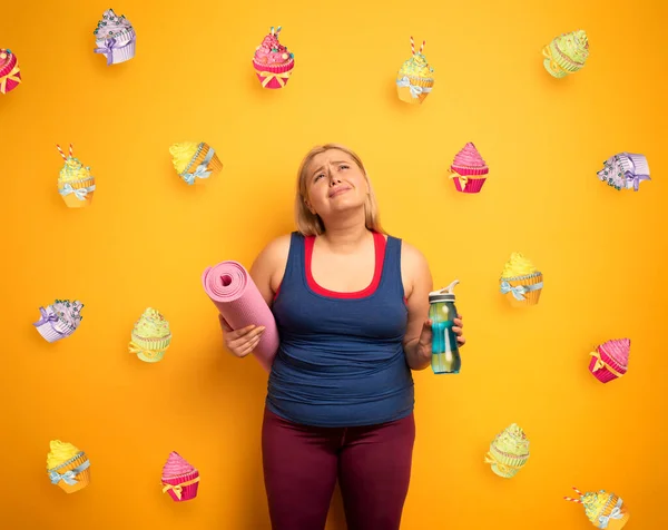 A gorda pensa em comer doces em vez de ir ao ginásio. fundo amarelo — Fotografia de Stock