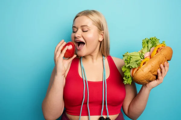 Şişman kız büyük bir sandviç yerine elma yemeyi tercih eder. cyan arkaplan — Stok fotoğraf