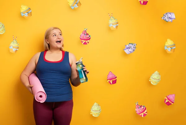 La gorda piensa en comer dulces en lugar de hacer gimnasia. fondo amarillo —  Fotos de Stock