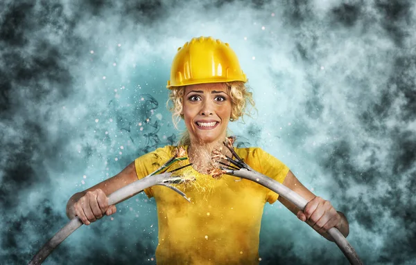 Werkster meisje met hoed breekt een elektrische kabel. Cyaan achtergrond — Stockfoto