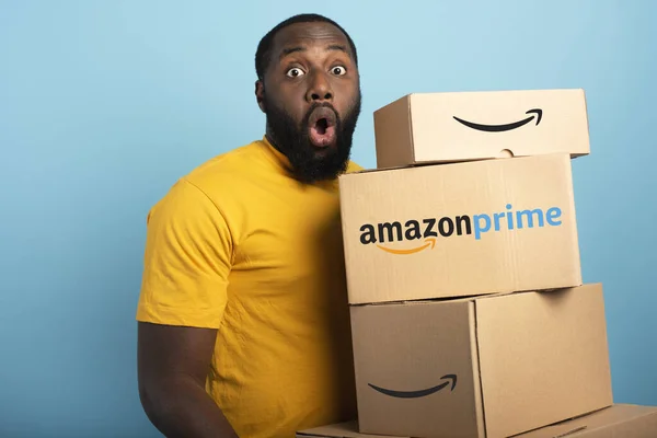 Surprised Man holds a lot of Amazon prime packages. Cyan background — Stock Photo, Image