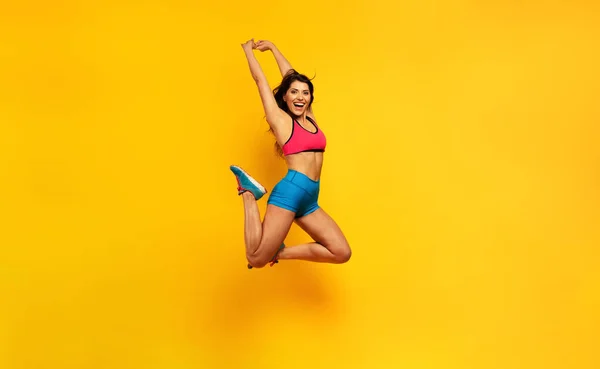 Sportovní žena skočí na žluté pozadí. Šťastný a radostný výraz. — Stock fotografie