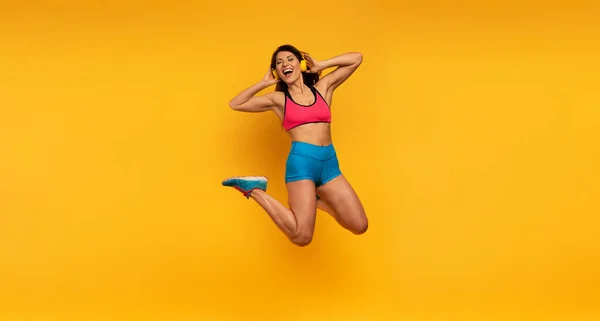Sport woman salta sobre un fondo amarillo y escucha música. Expresión feliz y alegre. —  Fotos de Stock