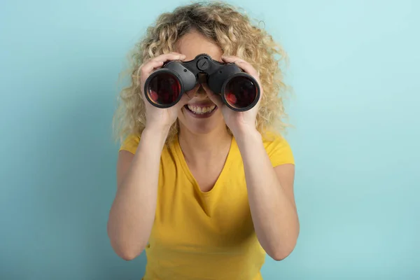 Ragazza felice guarda con binocolo qualcosa. Sfondo ciano — Foto Stock