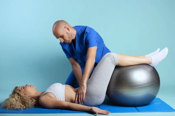 Meisje doet oefeningen met een fysiotherapeut. Cyaan achtergrond — Stockfoto