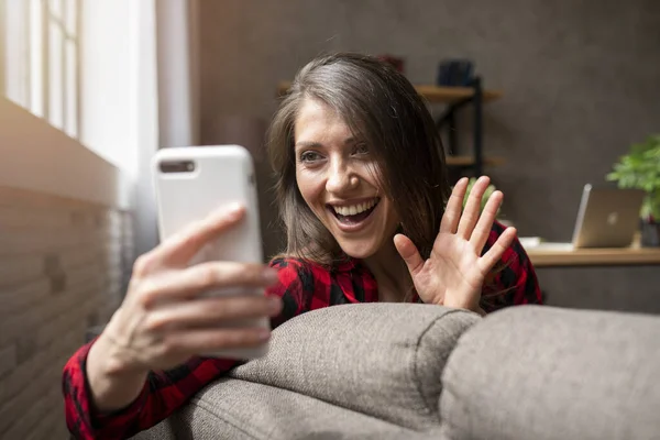 Девушка начинает видео-звонок со своего смартфона на диване — стоковое фото
