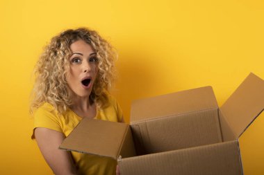 Mutlu kadın çevrimiçi mağaza siparişinden bir paket alır. Sarı arkaplan.