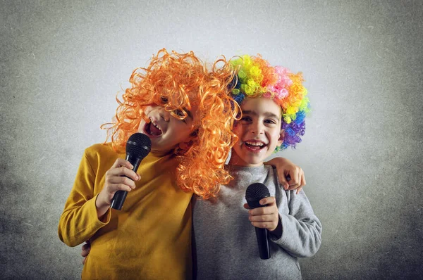 Dos niños cantan una canción con micrófono y peluca divertida — Foto de Stock