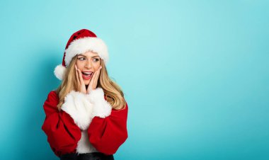 Noel Baba kostümlü, şaşırmış yüzlü bir kadın. cyan arkaplan