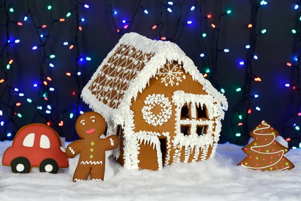 手作りの食べられるジンジャーブレッドハウス、小さな男、新年の木、車、雪の装飾、花輪の背景照明 — ストック写真