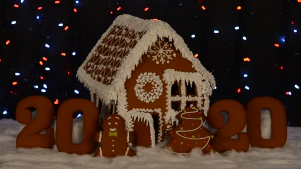 手作りの食べられるジンジャーブレッドハウス 2020年の碑文 小さな男 新年の木 雪の装飾 花輪の背景照明 — ストック動画