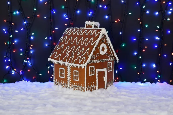 手作りの食べられるジンジャーブレッドハウス、雪の装飾、花輪の背景照明 — ストック写真