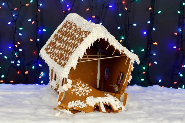 The crashed hand-made eatable gingerbread house, snow decoration, garland background illumination — Stock Photo, Image