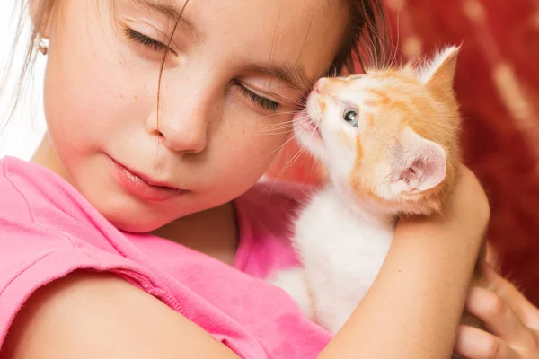 Ein kleines Mädchen hält ein Kätzchen auf dem Arm und umarmt es. — Stockfoto