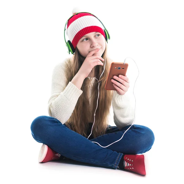 A felicidade das férias de inverno Natal. Conceito adolescente - jovem sorridente de chapéu vermelho com smartphone e fones de ouvido está ouvindo música e em fundo branco . — Fotografia de Stock