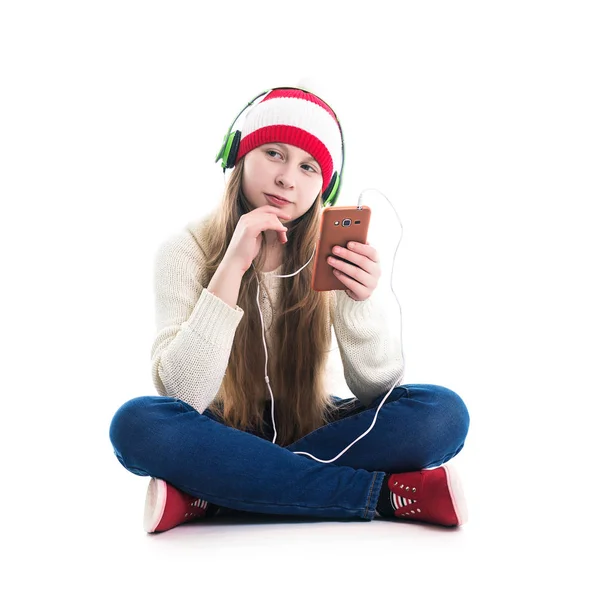 A felicidade das férias de inverno Natal. Conceito adolescente - jovem sorridente de chapéu vermelho com smartphone e fones de ouvido está ouvindo música e em fundo branco . — Fotografia de Stock