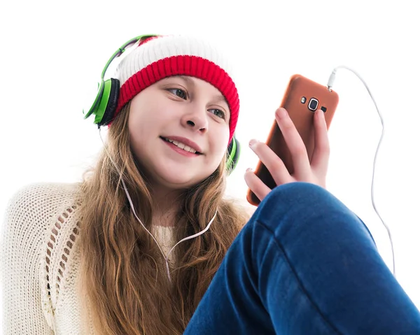 Szczęście święta Bożego Narodzenia. Koncepcja nastolatek - uśmiechnięta młoda kobieta w czerwonym kapeluszu z smartphone i słuchawki jest słuchanie muzyki i na białym tle. — Zdjęcie stockowe