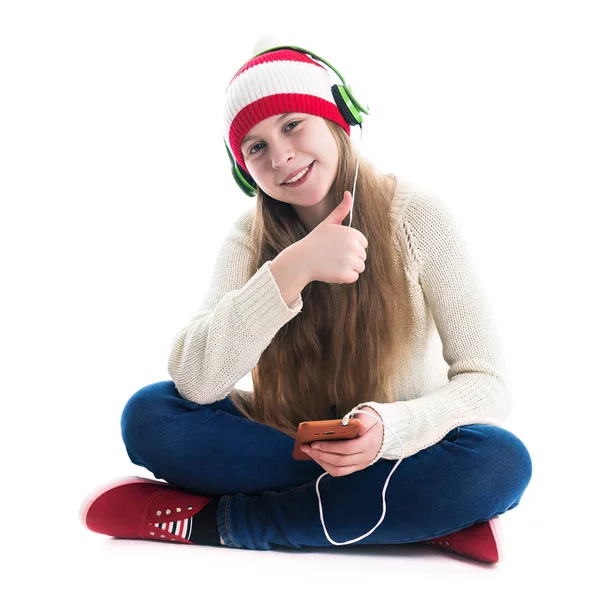 La felicidad de las vacaciones de invierno Navidad. Concepto adolescente: una joven sonriente con sombrero rojo con teléfono inteligente y auriculares escucha música y sobre un fondo blanco . — Foto de Stock