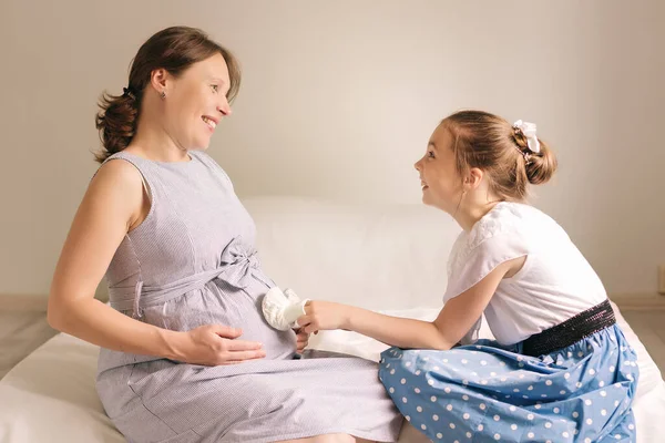 Gyönyörű terhes nő és az aranyos kislánya mosolyognak, miközben együtt töltik az időt otthon.. — Stock Fotó