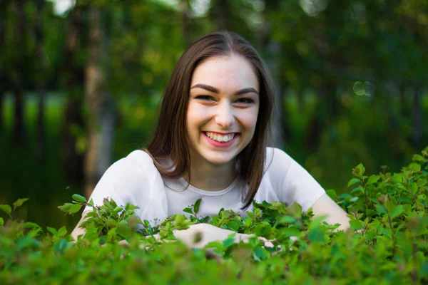 Retrato de uma bela jovem mulher em um fundo de folhas verdes, verão ao ar livre. Mulher naturalmente bonita sorrindo enquanto está entre as folhas verdes . — Fotografia de Stock