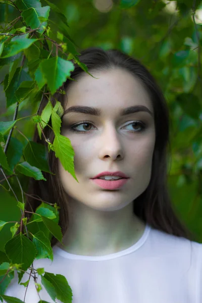 Portret van een mooie jonge vrouw op een achtergrond van groene bladeren, zomer buitenshuis. Natuurlijk mooie vrouw die lacht terwijl je onder de groene bladeren. — Stockfoto