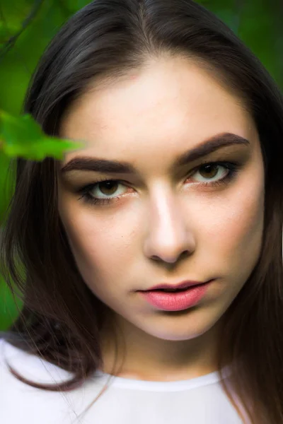 Portret van een mooie jonge vrouw op een achtergrond van groene bladeren, zomer buitenshuis. Natuurlijk mooie vrouw die lacht terwijl je onder de groene bladeren. — Stockfoto