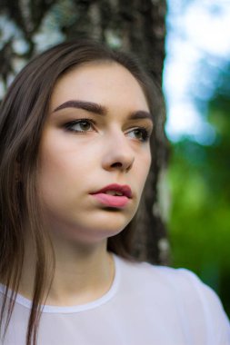 Yeşil yaprakları, yaz açık havada bir arka plan üzerinde güzel bir genç kadının portresi. Doğal olarak duran yeşil yaprakları arasında gülümseyen güzel kadın.