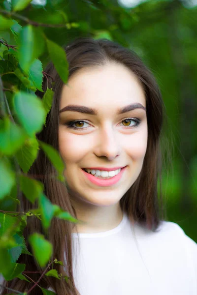 Portret pięknej młodej kobiety na tle zielonych liści, lato na zewnątrz. Naturalnie piękna kobieta uśmiechając się stojąc wśród zielonych liści. — Zdjęcie stockowe