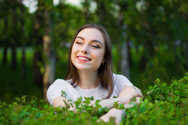 Portrait of a beautiful young woman on a background of green leaves, summer outdoors. Naturally beautiful woman smiling while standing among the green leaves. — Stock Photo, Image