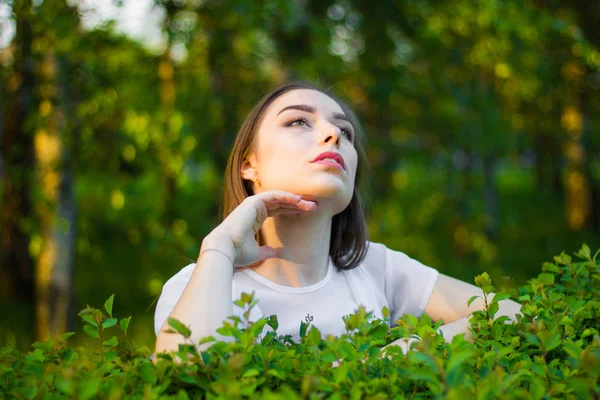 Portret van een mooie jonge vrouw op een achtergrond van groene bladeren, zomer buiten. — Stockfoto